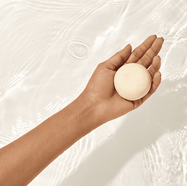 A hand holding a shampoo bar on a background with water