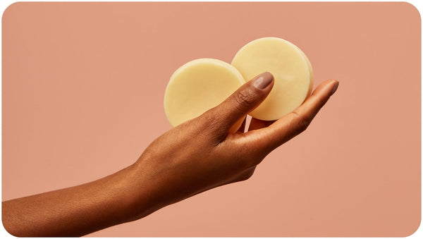 Woman who knows how to use conditioner bar holds two pieces of Bars Over Bottles conditioner bars