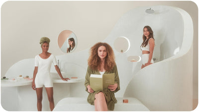 Vegan shampoo and conditioner bars and two women in white behind a woman in green robe holding a book